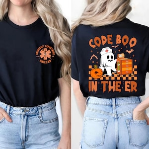 May include: Black t-shirt with a ghost wearing a nurse's hat and holding a stethoscope. The text "CODE BOO IN THE ER" is printed on the back of the shirt. The front of the shirt has a small embroidered patch with a medical symbol and the text "EMERGENCY DEPARTMENT EMILY.RN".