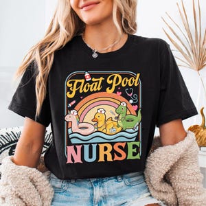 May include: Black t-shirt with a colorful graphic that reads "Float Pool Nurse." The design features cartoon floats shaped like a pink flamingo, a yellow duck, and a green dinosaur, all wearing nurse hats.