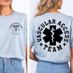 May include: Light blue t-shirt with black text and graphics. The front features a medical symbol and the words "VASCULAR ACCESS TEAM" and "Christina". The back displays a large black medical symbol with the words "VASCULAR ACCESS TEAM".