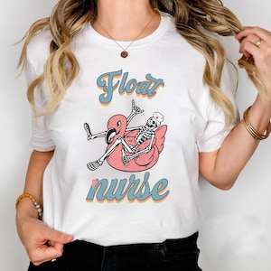 May include: White t-shirt featuring a pink flamingo float with a skeleton wearing a nurse's hat. The text "Float Nurse" is written in a retro font.