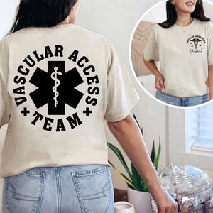 May include: Beige t-shirt with "VASCULAR ACCESS TEAM" printed in black around a black medical symbol on the back. The front of the shirt has a smaller matching design. The shirt is a crew neck.