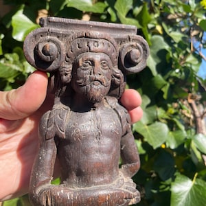 May include: A dark brown wooden sculpture of a man's torso with a carved face and a crown. The sculpture is carved in a detailed style and has a weathered finish.