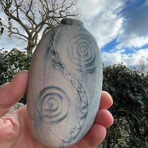 May include: A small, white ceramic vase with a blue glaze and a swirling pattern. The vase is oval shaped and has a narrow neck.