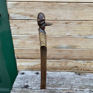 May include: A wooden carving of a person with a large nose and a hat. The carving is brown and has a rough texture. It is standing on a wooden surface.