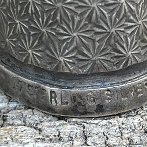 May include: Close-up of a silver thimble with a geometric pattern and the inscription "Sterling Silver" on the bottom.