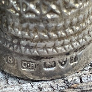 May include: Close-up of the bottom of a silver thimble with the number 8, the letters "CRT", and a maker's mark.