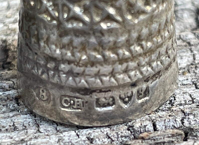 May include: Close-up of the bottom of a silver thimble with the number 8, the letters "CRT", and a maker's mark.