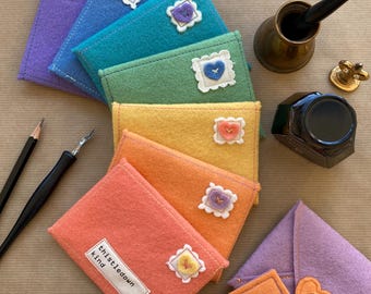 May include: A set of seven rainbow felt envelopes with heart-shaped buttons and the text "thistle down kind" on one envelope.