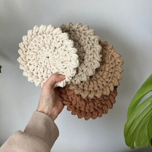 Op de afbeelding: Set van drie gehaakte onderzetters in beige, lichtbruin en bruin. De onderzetters zijn rond en hebben een textuur.