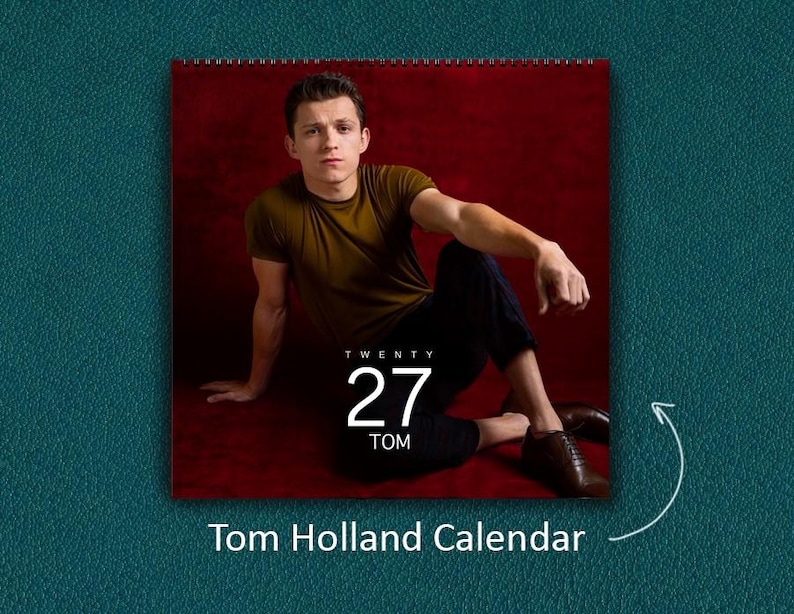 K&ouml;nnte beinhalten: Ein Wandkalender mit einem Foto von Tom Holland, der ein olivgr&uuml;nes T-Shirt und eine dunkle Hose vor einem tiefroten Hintergrund tr&auml;gt. Das Kalenderblatt zeigt den Text TWENTY 27 TOM in wei&szlig;er Schrift mittig &uuml;ber dem Bild platziert.