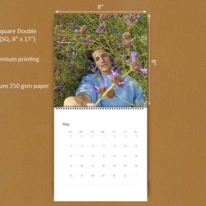 May include: A square double wall calendar measuring 8 inches by 17 inches, printed on 250 gsm paper. The top section features a photograph of a person in a blue sweater amidst purple flowers. The bottom section displays a May calendar grid.