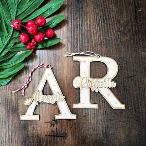 Op de afbeelding: Twee houten kerstversieringen in de vorm van de letters A en R. De letter A heeft de naam Alessio erop geschreven en de letter R heeft de naam Raffaella erop geschreven.
