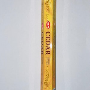May include: A rectangular box of HEM Cedar incense sticks. The box is a golden yellow color with decorative swirls and the word "CEDAR" in large, bold letters. The brand name "HEM" is also visible.