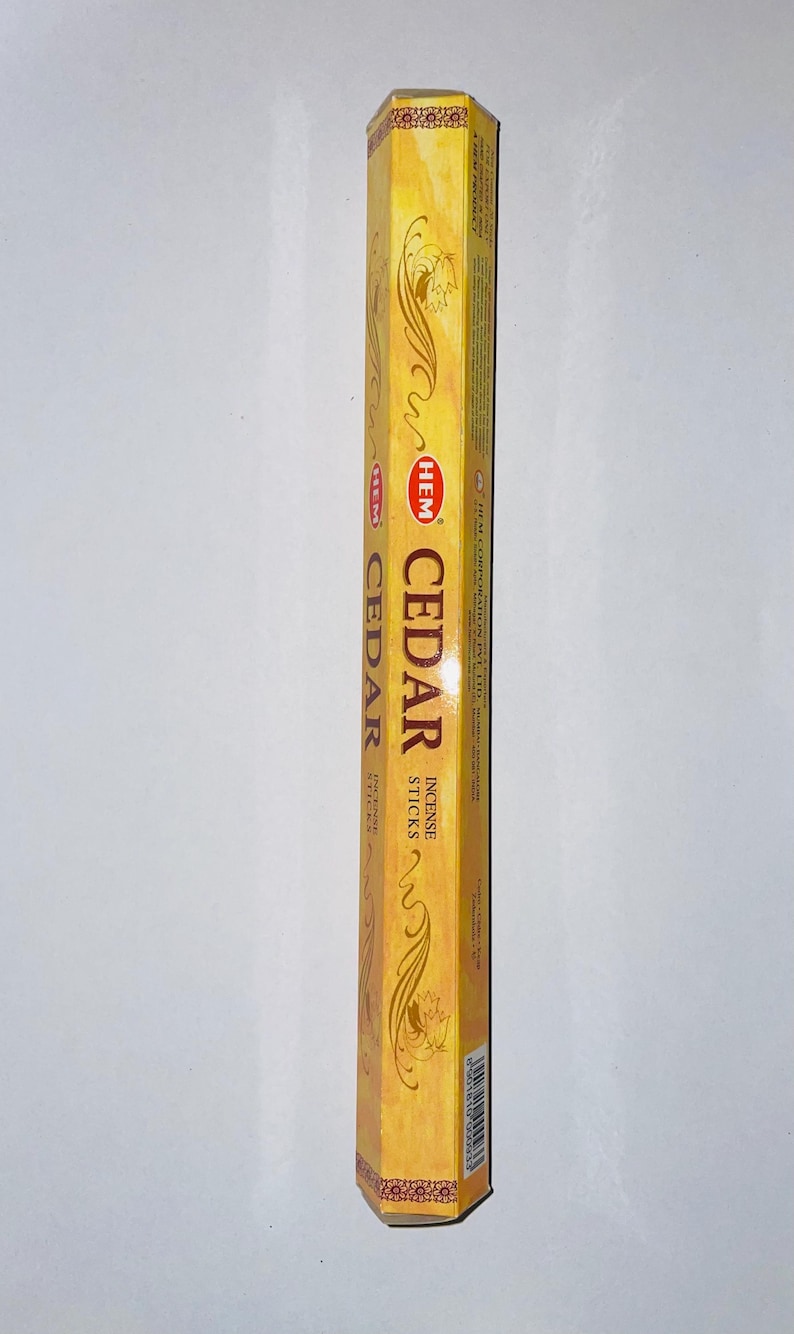 May include: A rectangular box of HEM Cedar incense sticks. The box is a golden yellow color with decorative swirls and the word "CEDAR" in large, bold letters. The brand name "HEM" is also visible.