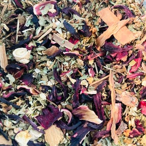 Könnte beinhalten: Nahaufnahme einer Mischung aus getrockneten Kräutern und Blüten, darunter Hibiskus, Zimtstangen und grüne Blätter. Die Mischung ist in leuchtenden Rot-, Braun- und Grüntönen.