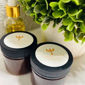 May include: Two black jars of brown balm with white labels that say "Anuket's Blending Balm" with a gold Egyptian goddess design.