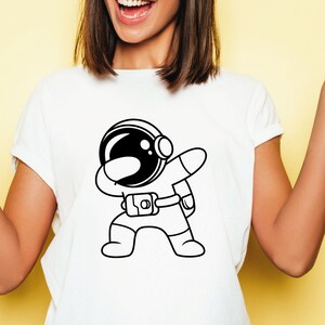 K&ouml;nnte beinhalten: Wei&szlig;es T-Shirt mit einer schwarz-wei&szlig;en Illustration eines Astronauten, der den Dab macht.