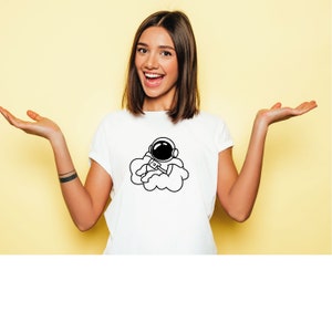 K&ouml;nnte beinhalten: Wei&szlig;es T-Shirt mit einer schwarz-wei&szlig;en Illustration eines Astronauten, der in einer Wolke schwebt.