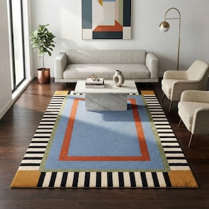 May include: A rectangular area rug featuring a central light blue field bordered by a bold orange rectangle and a thin green frame. The outer edges display a black and white striped pattern with solid mustard yellow corner squares on the rug.