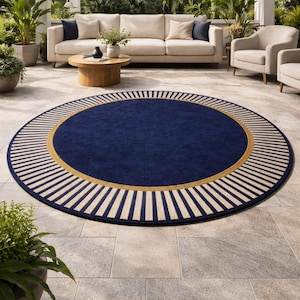 May include: A round navy blue rug with a gold border and cream-colored stripes. The rug is placed on a stone patio, with outdoor furniture and greenery in the background. The rug's diameter is approximately 8 feet.