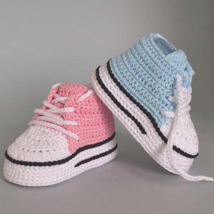 May include: A pair of handmade crochet baby trainers. One is pink and white, the other is blue and white. Both have white laces, black stripes, and a white sole. These soft shoes are a charming gift for a newborn.