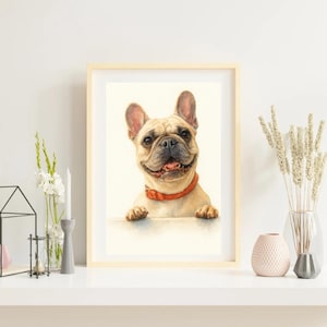Può includere: Una stampa ad acquerello incorniciata di un bulldog francese sorridente con un collare rosso. Il pelo marrone chiaro e l'espressione felice del cane sono il punto focale. L'opera d'arte è esposta su una superficie bianca, con oggetti decorativi sullo sfondo.