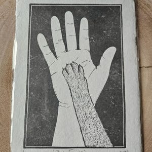 May include: A black and white linocut print of a human hand and a cat paw touching. The print is titled "Best Friends" and numbered 1/50.
