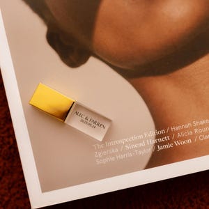 Op de afbeelding: Een rechthoekige USB-stick met een metallic gouden dop en een behuizing van helder acryl. Het doorzichtige gedeelte is bedrukt met de tekst ALEC & FARREN en de datum 2025.05.24 in een strak, zwart schreefloos lettertype, geplaatst op een pagina.