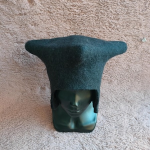 May include: A dark teal felt hat with a unique, angular design. The hat has a wide, flat brim and a tall, pointed crown. The hat is displayed on a dark green mannequin head.