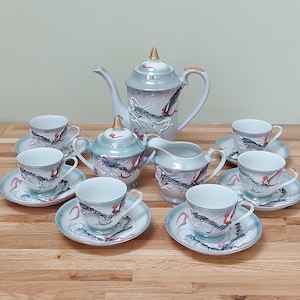 May include: A complete porcelain tea set with a teapot, creamer, sugar bowl, and six teacups with saucers. The set is light blue with a dragon design and gold accents. The teapot measures approximately 25 cm in height.