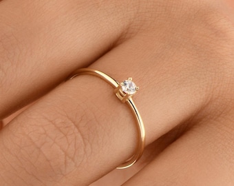 May include: A delicate gold ring with a single, small, clear gemstone.