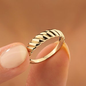 May include: A gold ring with a textured, ridged design. The ring is shown on a finger.