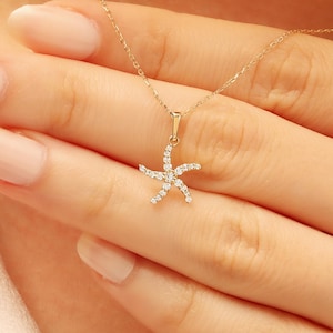 May include: A gold-colored necklace featuring a starfish pendant adorned with small, sparkling gemstones. The starfish design is delicate and detailed, suspended from a fine chain. The necklace is shown against a skin tone background.