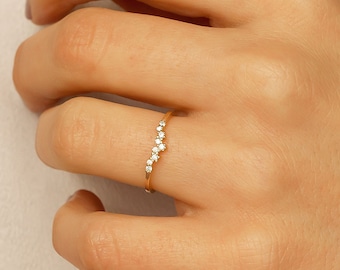 Puede incluir: Un delicado anillo de banda de oro con una fila curva de pequeñas piedras preciosas transparentes.