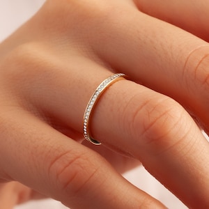 May include: A thin gold band ring with a row of small diamonds set around the entire band.