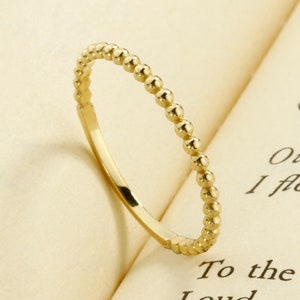 May include: A delicate gold ring with a beaded design. The ring is thin and has a simple, elegant style.