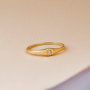 May include: A gold ring with a small diamond set in a starburst design.