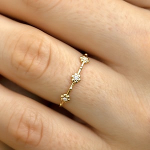 Könnte beinhalten: Ein zarter Goldring mit einer Reihe kleiner blütenförmiger Akzente, die jeweils mit einem winzigen Diamanten besetzt sind.