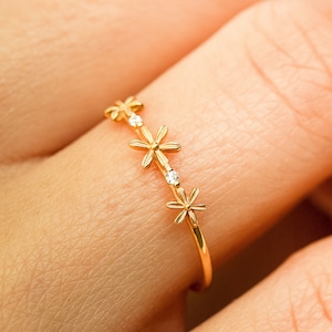 May include: A gold ring with three delicate flower designs, each with a small clear stone in the center.