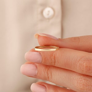 May include: A thin gold band ring, shown on a finger.
