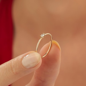 May include: A delicate gold ring with a single, small, clear gemstone.