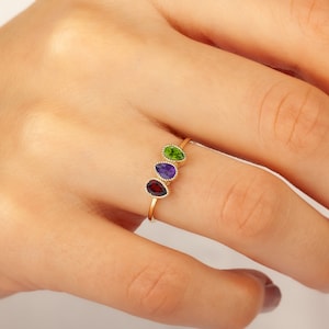 May include: A gold ring with three pear-shaped gemstones. The gemstones are red, purple, and green.