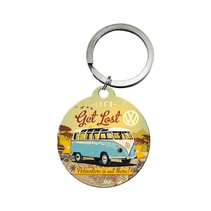 Könnte beinhalten: Ein runder Schlüsselanhänger aus Metall mit einer Vintage-Illustration eines blauen Volkswagen-Busses mit dem Text "Let's Get Lost" und "Adventure is out there!" Der Schlüsselanhänger enthält auch ein Volkswagen-Logo.