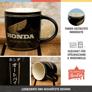 K&ouml;nnte beinhalten: Schwarze Honda Motorcycles Keramik-Tasse mit goldenem Fl&uuml;gel-Logo und Text. Die Tasse hat einen schwarzen Henkel und eine cremefarbene Innenseite. Der Text "HONDA MOTORCYCLES" ist wei&szlig;.