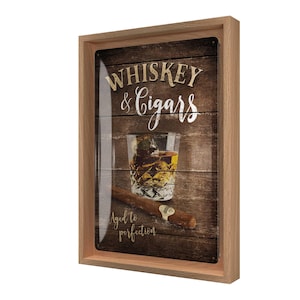 Könnte beinhalten: Holzgerahmtes Wandbild mit Whiskey- und Zigarren-Motiv. Das Kunstwerk zeigt ein Glas Whiskey mit Eis, eine Zigarre und die Worte "Whiskey & Cigars" und "Aged to perfection" in weißer Schrift auf einem Holzmaserungshintergrund.