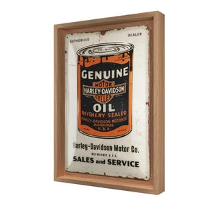 Könnte beinhalten: Gerahmtes Vintage Harley-Davidson Ölschild. Das Schild hat einen Used-Look mit den Worten "GENUINE MOTOR HARLEY-DAVIDSON CYCLES OIL" in Schwarz und Orange. Das Schild befindet sich in einem hellbraunen Holzrahmen.