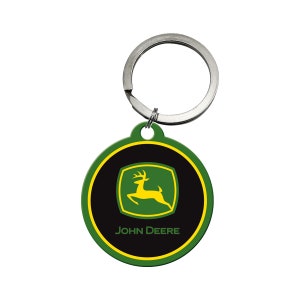 Könnte beinhalten: Ein runder Schlüsselanhänger in Grün und Schwarz mit einem silbernen Ring. Der Schlüsselanhänger zeigt das John Deere Logo, das ein springendes Reh in Gelb vor grünem Hintergrund beinhaltet.