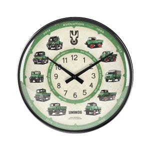Könnte beinhalten: Runde Wanduhr mit schwarzem Rahmen und grün-cremefarbenem Zifferblatt. Die Uhr zeigt Illustrationen grüner Unimog-Lastwagen aus verschiedenen Jahren, mit dem Wort "EVOLUTION" oben und "UNIMOG" unten.
