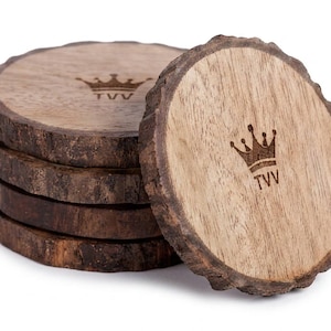 Pode incluir: Uma pilha de cinco porta-copos circulares de madeira com bordas de casca natural. Cada porta-copos apresenta uma superfície superior lisa e castanho-clara gravada com um ícone de coroa castanho-escura acima das letras TVV.