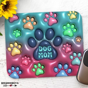 May include: A colorful mouse pad with a pink, blue, and green gradient background. The mouse pad is covered in paw prints and has the words "Dog Mom" in the center.